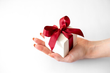 White box with red bow lies in awoman's hand on white background. Gift box in female hand