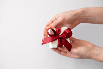 Female hands hold white box with red bow on grey background. Gift box in female hands