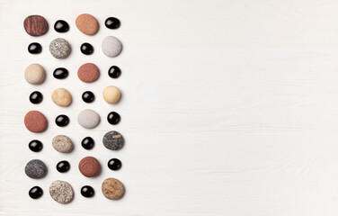 pattern of colored pebbles and black glass beads on white wooden background. Flat lay, top view