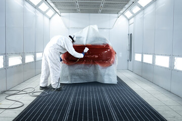 Painter applying new layer of fresh metallic paint on the automobile in painting chamber.