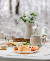 Obraz na płótnie Canvas Avocado toast, oranges, coffee on Breakfast table in snow cover backyard feels like winter wonderland