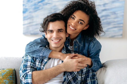 Portrait of a happy mixed race couple in love. Pretty african american curly girl and hispanic attractive guy tenderly hugging each other, looking at the camera, smiling, happy family