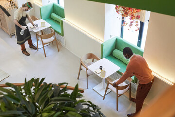 High angle view at two cafe workers cleaning tables and sanitizing furniture while preparing for opening in morning, copy space