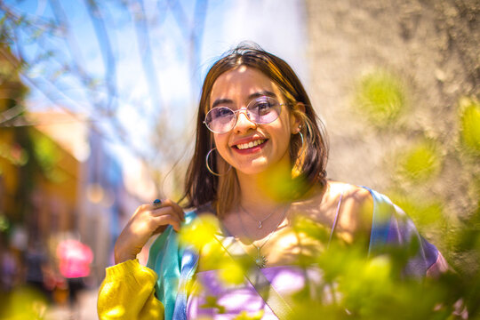 Daylight portrait of young handsome caucasian man isolated on grey background, dressed in white t-shirt and round eyeglasses, looking at camera and smiling positively, pensative serious men
