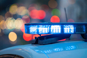 Blue lights on the roof of a police car with the background out of focus and lights with bokeh effect