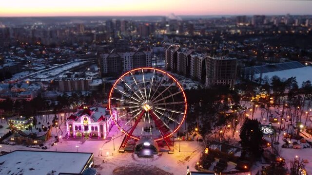  Aerial view on Ferris wheel. Drone fly left to right in winter Kharkiv city center. Amusement Gorky Central Park in sunset. City lights, streets with blurred effect