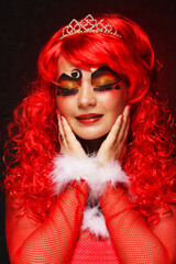 Charming woman in red curly wig and crown. The princess smiles.