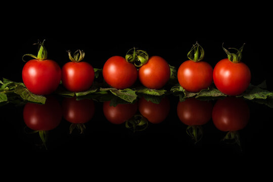 Delicious cherry tomatoes with leaves isolated on a black background with reflection. Horizontal image with copy space.