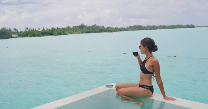 Coffee Luxury lifestyle concept. Woman drinking coffee relaxing wearing bikini in infinty pool looking at view of ocean. Travel vacation Luxury living at resort or expensive private villa.