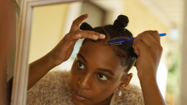 teenager in bantu knots looks into mirror while laying edges down