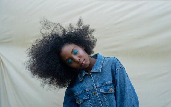 young girl with afro hair and denim jacket bends head in the wind
