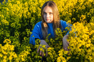 Fototapeta premium Young blonde girl in a field of rapeseed at sunset