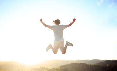 Man jumping and celebrating with arms raised with sunset in the background. Man jumping for joy, feeling happy and free.