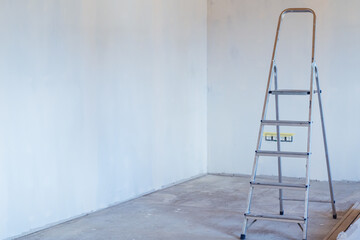 Metal stepladder in room with concrete floor and plastered walls. Home renovation and improvement