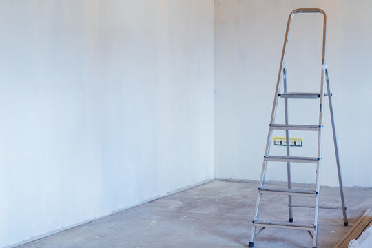 Metal stepladder in room with concrete floor and plastered walls. Home renovation and improvement