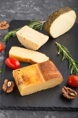 Smoked cheese and various types of cheese with rosemary and tomatoes on black slate board on a black concrete background. Side view, selective focus.