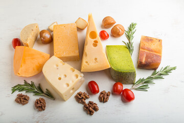 Set of different types of cheese with rosemary and tomatoes on a white wooden background . Side view.