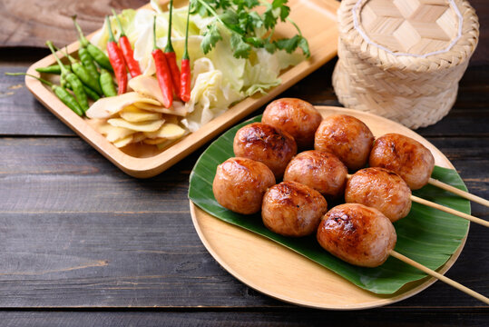 Thai sausage or Isan sausage (grilled fermented rice with minced pork) eating with fresh cabbage, ginger, and chili peppers on wooden background