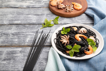 Black cuttlefish ink pasta with shrimps or prawns and small octopuses on gray wooden background. Side view, copy space.