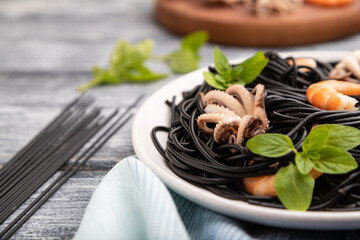 Black cuttlefish ink pasta with shrimps or prawns and small octopuses on gray wooden background. Side view, selective focus.