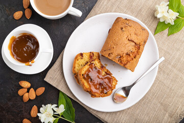 Homemade cake with raisins, almonds, soft caramel and a cup of coffee on a black concrete background. top view, close up.