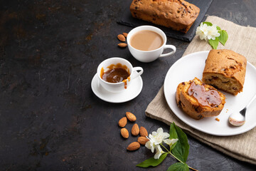 Homemade cake with raisins, almonds, soft caramel and a cup of coffee on a black concrete background. Side view, copy space.