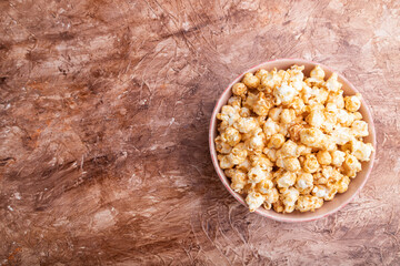 Popcorn with caramel in ceramic bowl on brown concrete background. Top view, copy space.