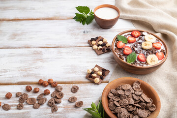 Chocolate cornflakes with milk and strawberry in wooden bowl on white wooden background. Side view, copy space.