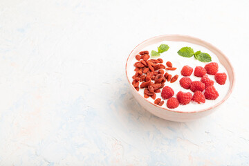 Yogurt with raspberry and goji berries in ceramic bowl on white concrete background. Side view, copy space.