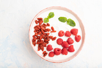 Yogurt with raspberry and goji berries in ceramic bowl on white concrete background. top view.