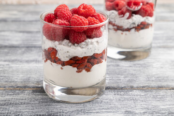 Yogurt with raspberry, goji berries and chia seeds in glass on gray wooden background. Side view, selective focus.