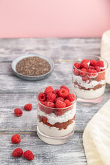 Yogurt with raspberry, goji berries and chia seeds in glass on gray wooden background. Side view, selective focus.