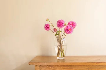 Foto op Plexiglas Close up of bright pink dahlias in glass vase on oak side table against beige wall © Natalie Board