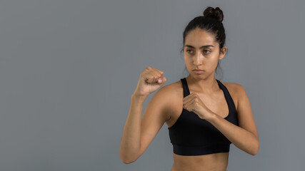 Fototapeta na wymiar Joven mujer latina mexicana atleta entrenando artes marciales: taekwondo, karate, box. Vestida de negro y haciendo ejercicio con fondo gris