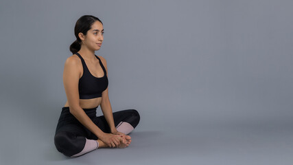 Fototapeta premium Joven mujer latina mexicana atleta instructora entrenando yoga dando calentamiento y estiramiento de musculos vestida de negro y haciendo ejercicio con fondo gris en pandemia por covid 19 coronavirus