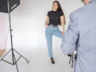 Fototapeta na wymiar Photographer takes pictures of the model in the studio. View from the back. The model is out of focus. Lighting equipment.