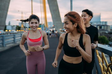 Happy Asian female and male friends in sportswear running and jogging at city bridge for a fit and healthy lifestyle - friendship and healthy concept