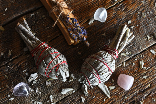 A top view image of two sage smudge sticks and healing crystals on a dark wooden table top. 