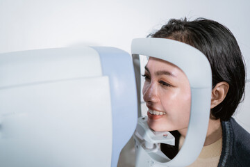 A woman is undergoing an examination using an eye examiner computer in an eye clinic room