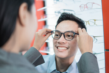 a lady shop assistant puts new glasses on to a male customer at an optician
