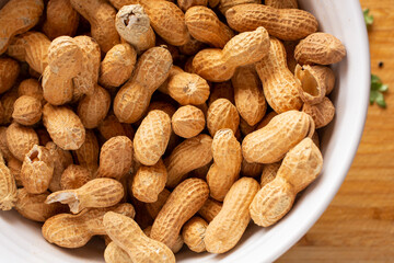 A top down view of a bowl of peanuts in their shells.