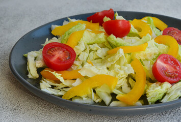 fresh summer salad of peking cabbage, yellow sweet bell pepper and cherry tomato in a ceramic plate, vegetarian food and diet