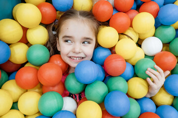 Fototapeta na wymiar a child in the children's playroom. The girl is having fun among the colorful balls. Dry Pool Party