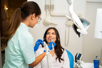 Professional dentist working in clinic, young adult brunette sitting in chair, modern clinic.