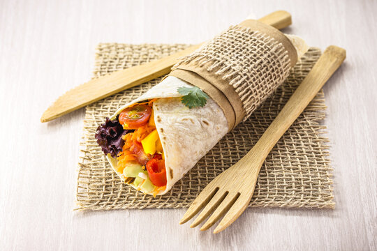 Vegan tortilla wrap, vegetarian roll with grilled vegetables, pepper, lentils, tomatoes and cabbage, on a rustic wooden background