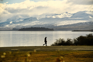 A woman walking by the lake And the background is snowy mountains in Lake Tekapo, South Island, New Zealand.