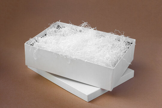 white shredded paper in a white open box on the lid on a paper beige background for protection during delivery, minimalism.