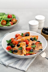 Baked perch fish fillets, italian style in crazy water with black olives, tomatoes and capers, with fresh parsley.