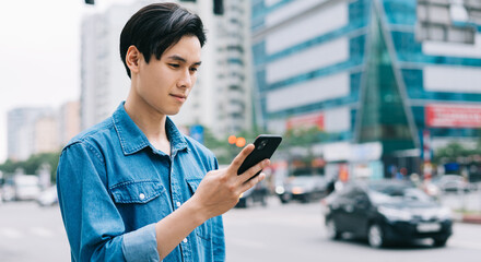 Fototapeta na wymiar Young Asian man walking and using smartphone on the street