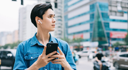 Young Asian man walking and using smartphone on the street
